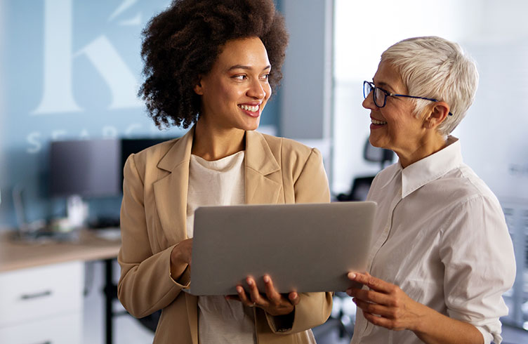 two HR recruiters working together in an office smiling over a laptop