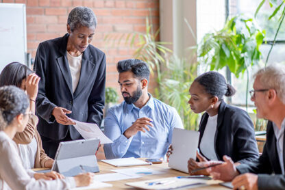 team of 6 people showing diversity in leadership standing around a conference table and computer