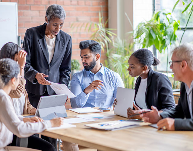 team of 6 people showing diversity in leadership standing around a conference table and computer