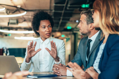 young Black woman leading a meeting at a conference table with two colleagues, a white man and woman