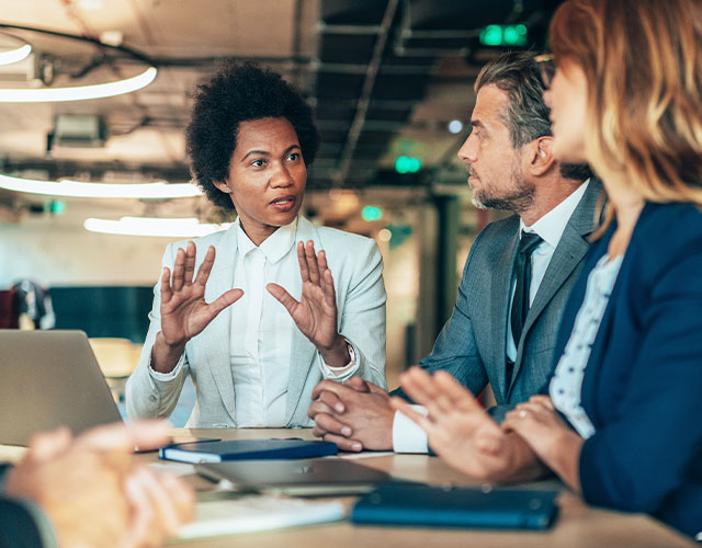 young Black woman leading a meeting at a conference table with two colleagues, a white man and woman
